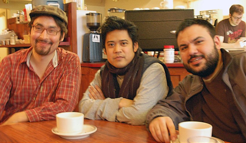 Three men sit at table with coffee cups