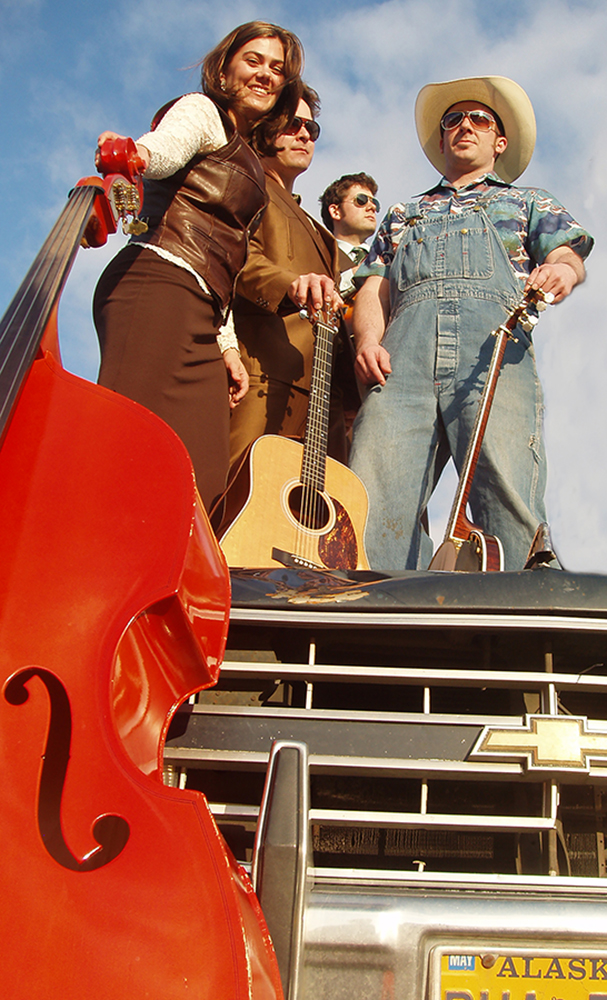 Musicians holding instruments stand on hood of truck